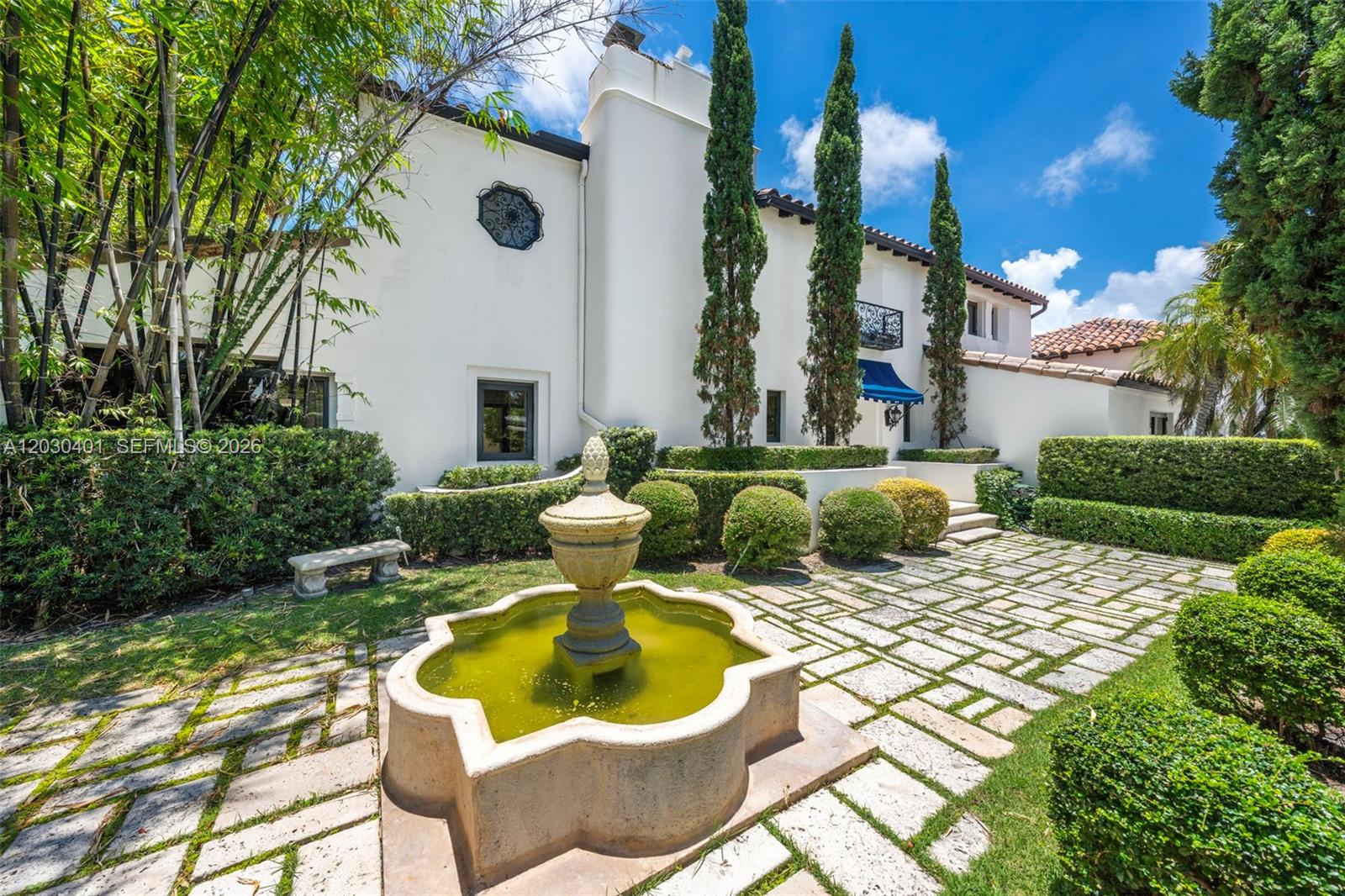 A stone fountain sits in a paved courtyard in front of a white stucco house — 5860 Pine Tree Dr, Miami Beach FL 33140, MIAMI BEACH, FL