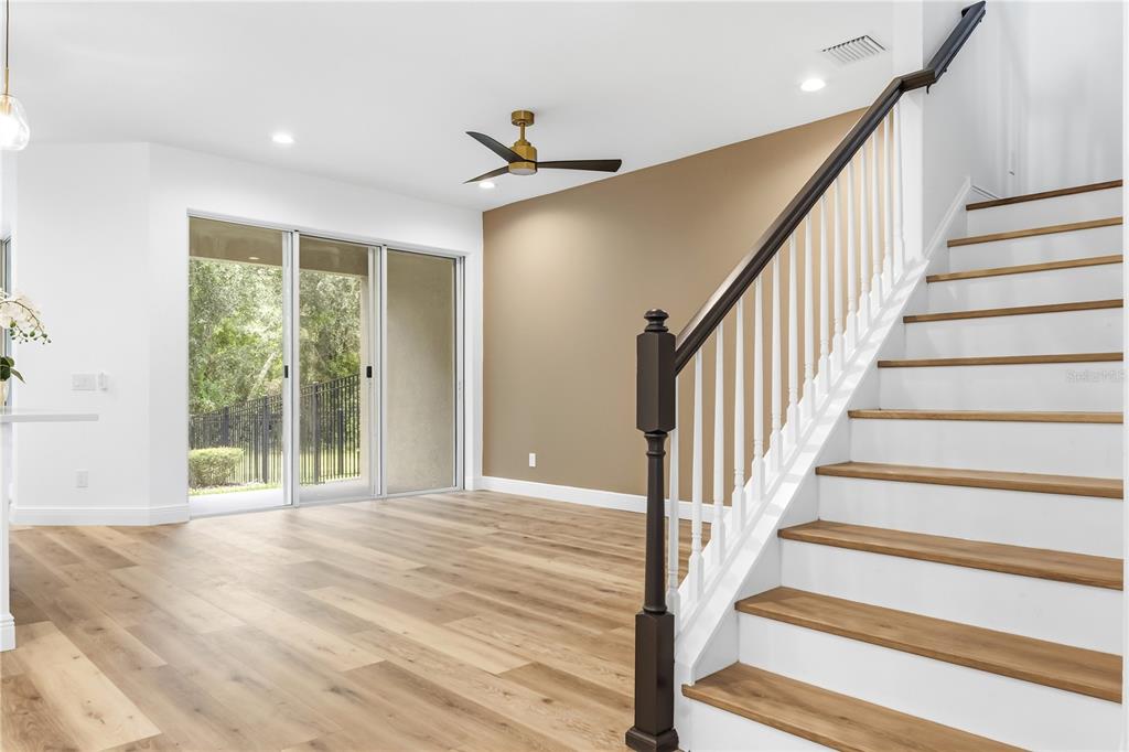 A room with light wood flooring, a staircase with dark railings, and sliding glass doors — 14409 MIRABELLE VISTA CIRCLE, TAMPA, FL