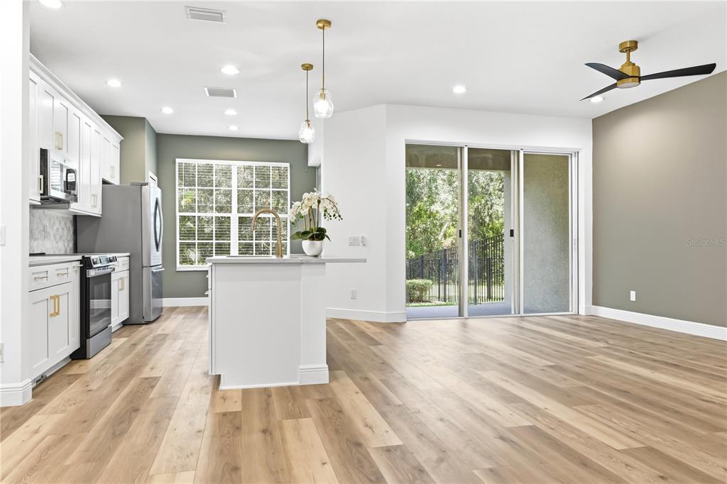 A modern kitchen with white cabinetry, a center island, and wood-look flooring opens to a patio — 14409 MIRABELLE VISTA CIRCLE, TAMPA, FL
