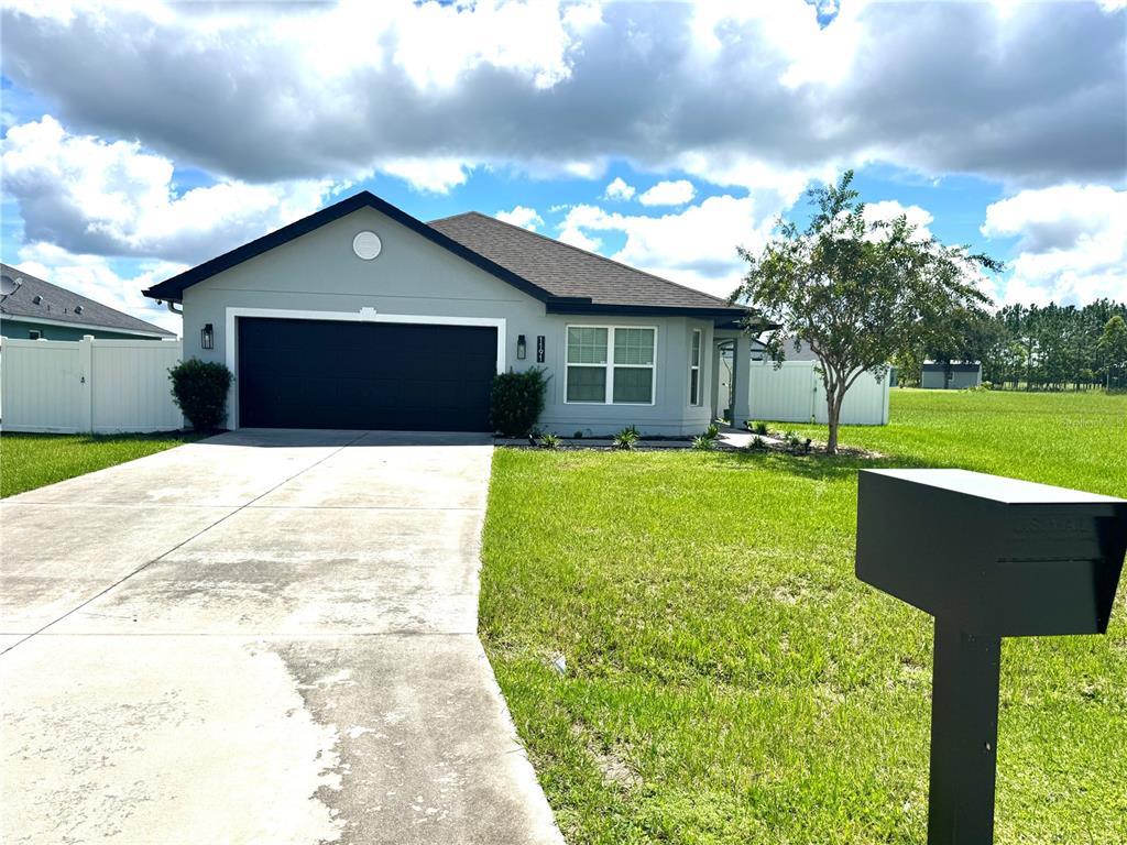 A single-story house with a gray exterior, black garage door, and a concrete driveway — 1191 SABINE LANE, KISSIMMEE, FL