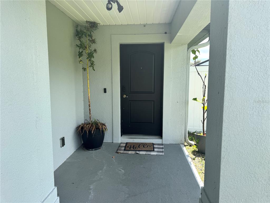 A covered front porch features a black door, a welcome mat, and two potted plants — 1191 SABINE LANE, KISSIMMEE, FL