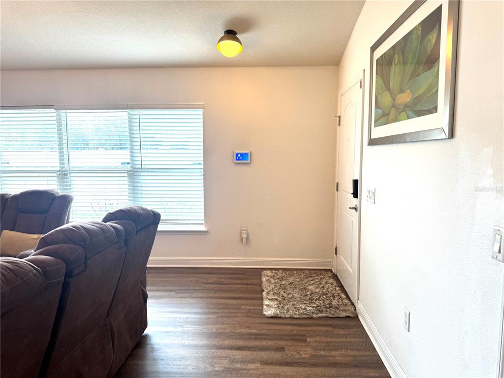 A living room features wood-look flooring, a brown sofa, a front door, and a wall-mounted thermostat — 1191 SABINE LANE, KISSIMMEE, FL