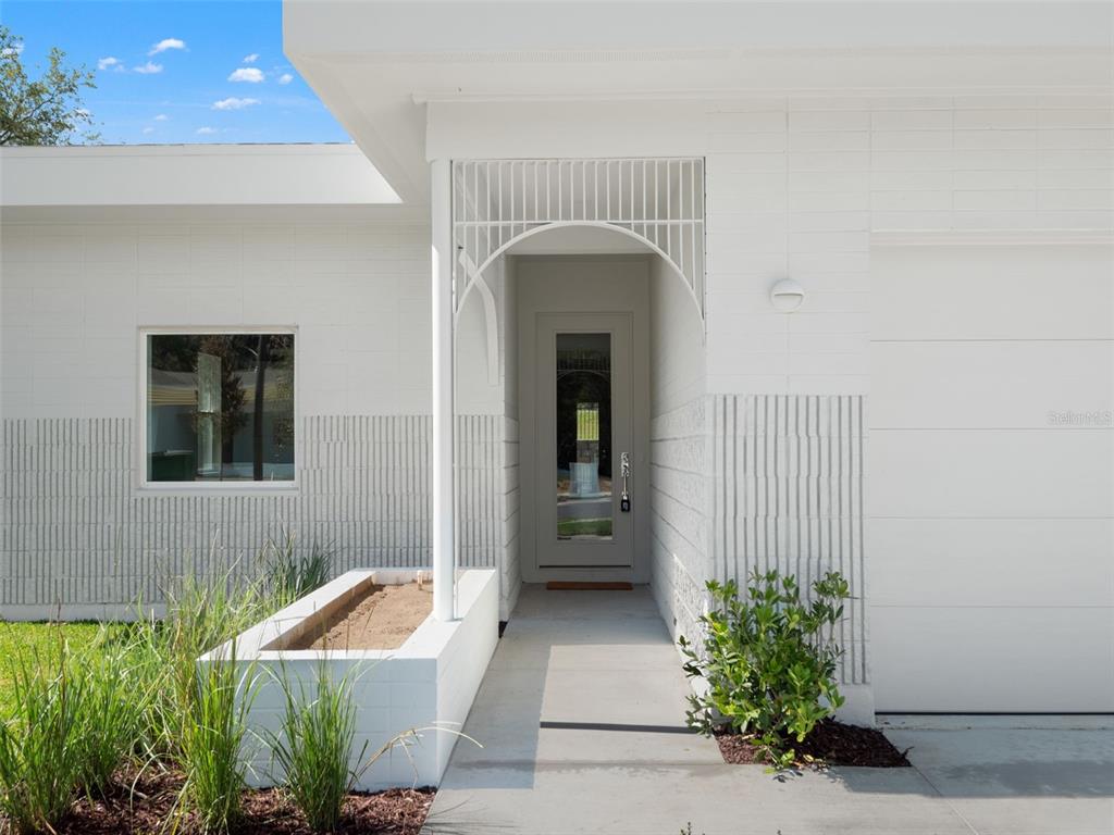A white exterior home entrance features a glass-paneled door, a decorative metal arch, and planters — 458 SKYFIELD COURT, LADY LAKE, FL