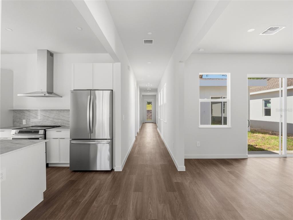 A kitchen with stainless steel appliances opens to a hallway and a sliding glass door — 458 SKYFIELD COURT, LADY LAKE, FL