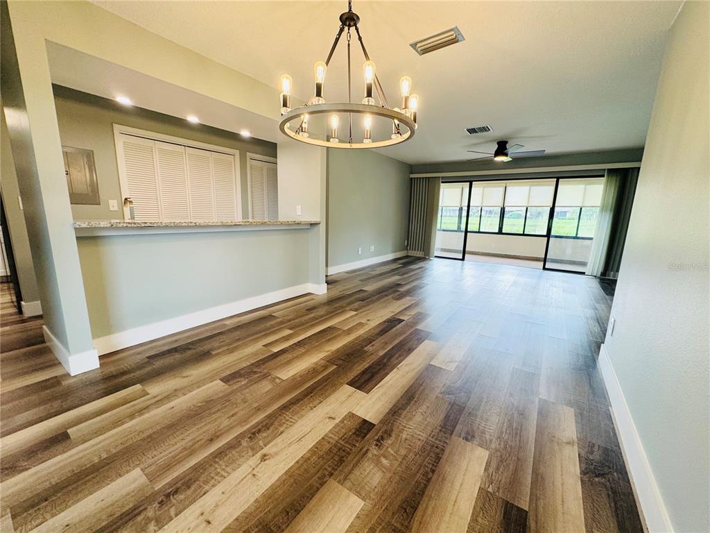An open living area features wood-look flooring, a kitchen pass-through, a chandelier, and sliding glass doors — 20 LAKE COURT, OLDSMAR, FL
