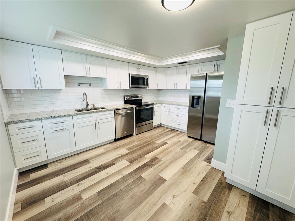 A kitchen with white cabinets, stainless steel appliances, granite countertops, and wood-look flooring — 20 LAKE COURT, OLDSMAR, FL