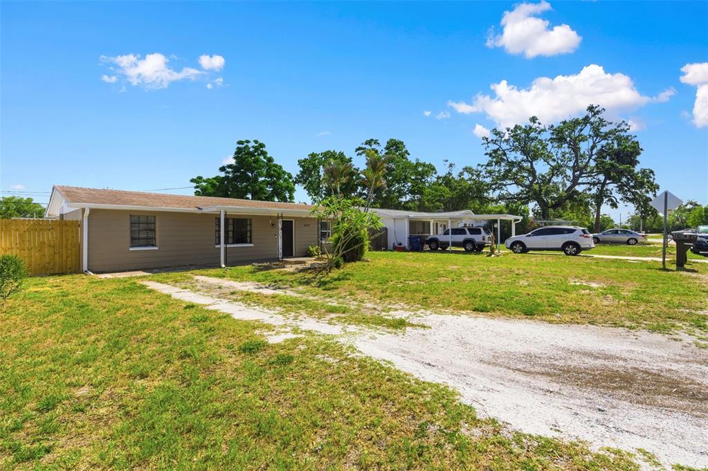 A single-story house with tan siding and a gravel driveway sits on a grassy lot — 4327 BEACON SQUARE DRIVE, HOLIDAY, FL