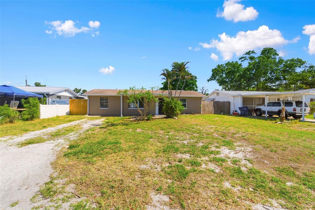 A single-story house with a tan exterior, a gravel driveway, and a white carport — 4327 BEACON SQUARE DRIVE, HOLIDAY, FL