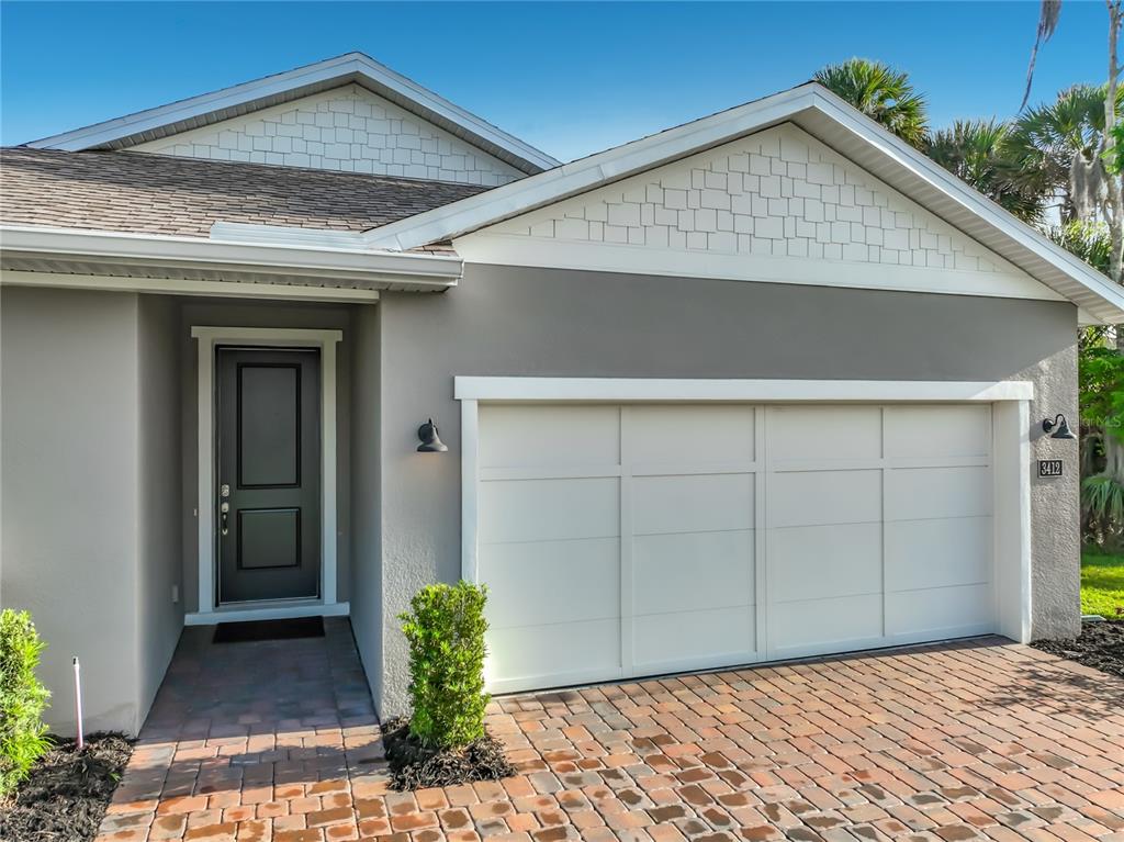 A gray house exterior features a white garage door, a dark front door, and brick pavers — 3412 BLUFF OAK LANE, SANFORD, FL
