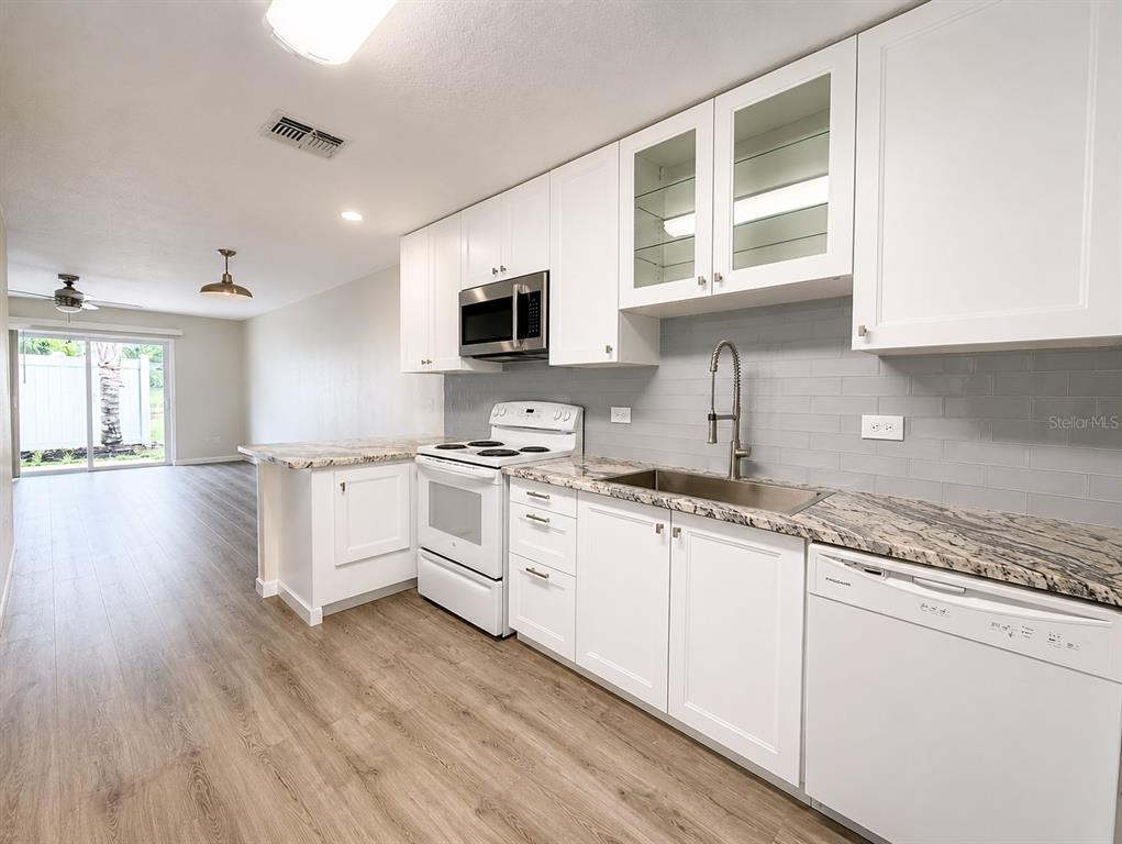 A kitchen with white cabinets, granite countertops, and stainless steel appliances opens to a living area — 238 RIDGECREST LOOP UNIT A, MINNEOLA, FL