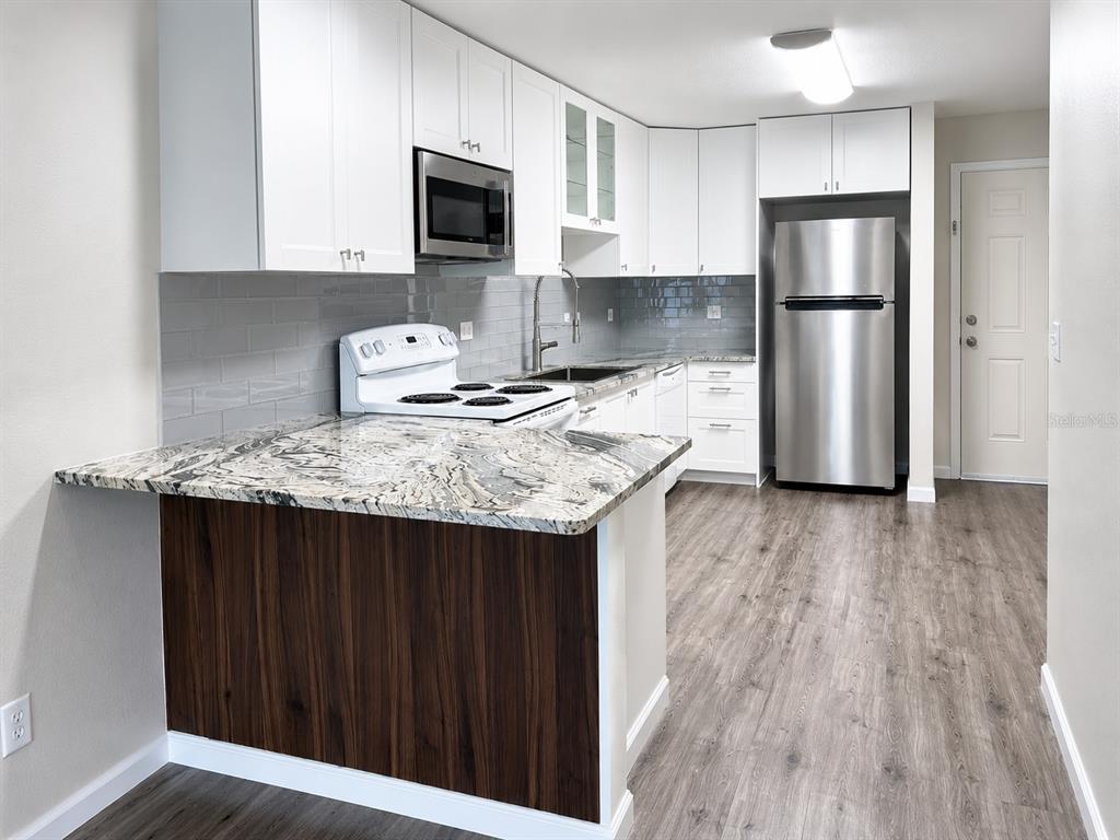 A kitchen features white cabinets, granite countertops, a stainless steel refrigerator, and wood-look flooring — 238 RIDGECREST LOOP UNIT A, MINNEOLA, FL