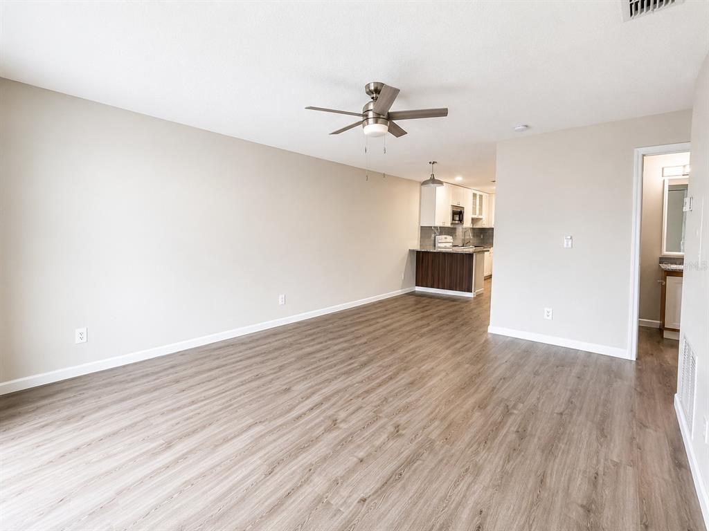 An open-concept living area features light-colored walls, wood-look flooring, a ceiling fan, and a kitchen — 238 RIDGECREST LOOP UNIT A, MINNEOLA, FL