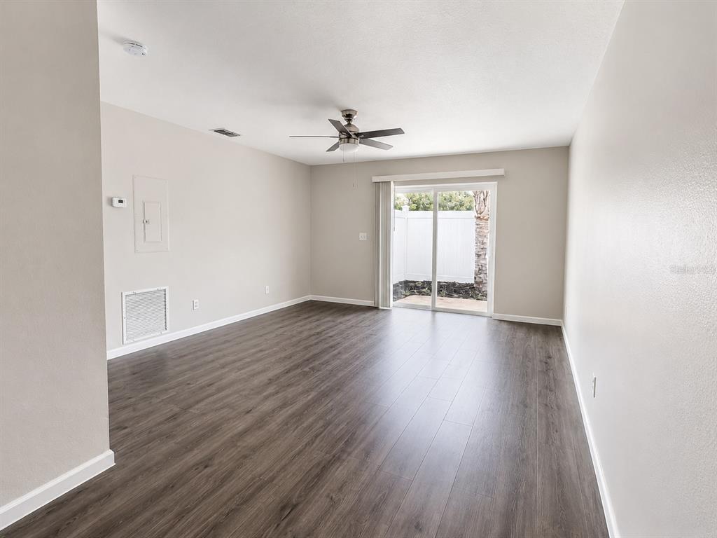 An empty living room with wood-look flooring, a ceiling fan, and a sliding glass door — 238 RIDGECREST LOOP UNIT A, MINNEOLA, FL