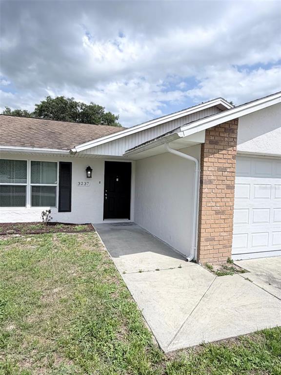 A single-story house exterior features a white stucco facade, brick accents, and a concrete walkway — 3237 LONDON AVENUE, DELTONA, FL