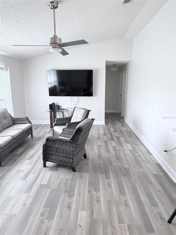 A living room features gray wood-look flooring, a ceiling fan, and wicker furniture — 3237 LONDON AVENUE, DELTONA, FL