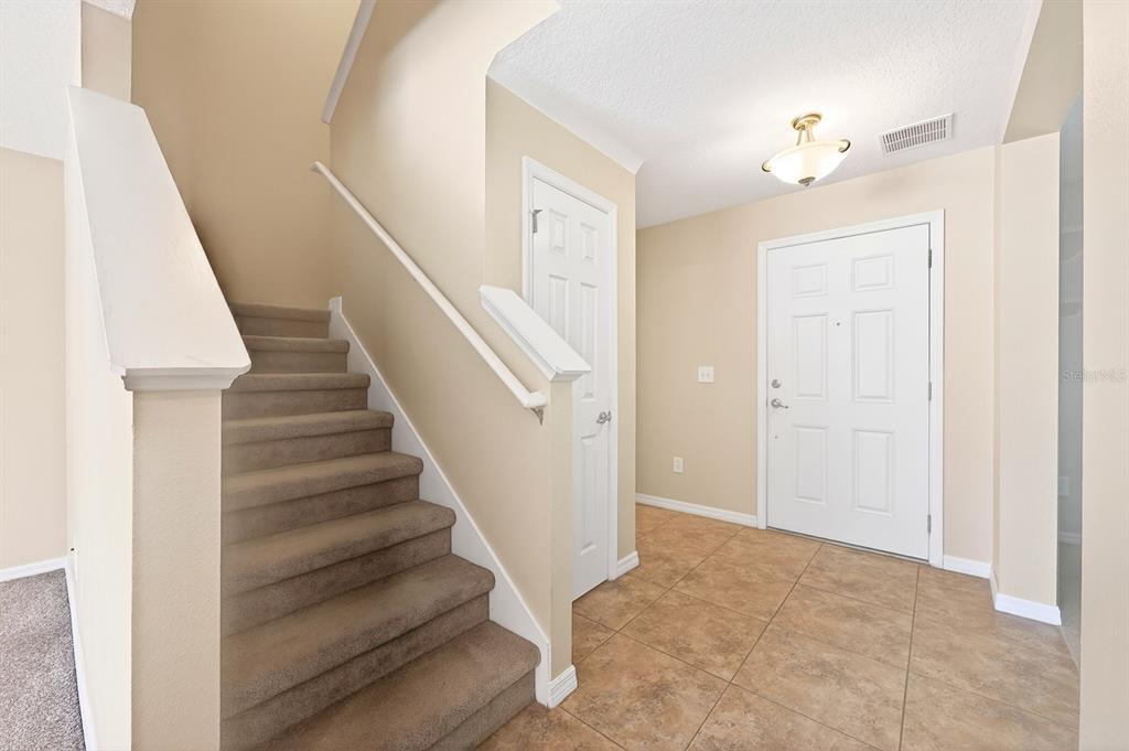 An entryway features a carpeted staircase, a white front door, and tan tile flooring — 2564 ABEY BLANCO DRIVE, ORLANDO, FL