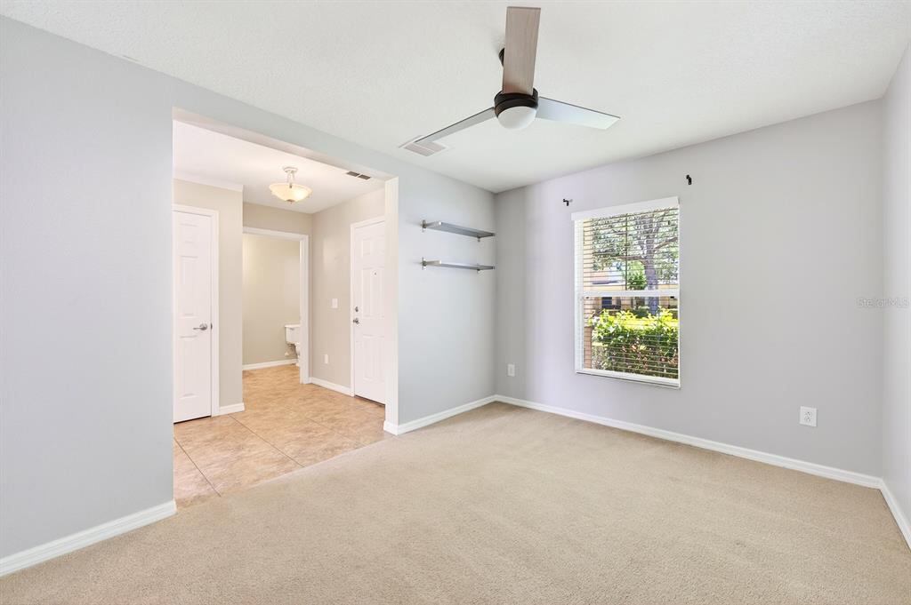A carpeted bedroom with a ceiling fan, two wall shelves, and an adjacent tiled hallway — 2564 ABEY BLANCO DRIVE, ORLANDO, FL