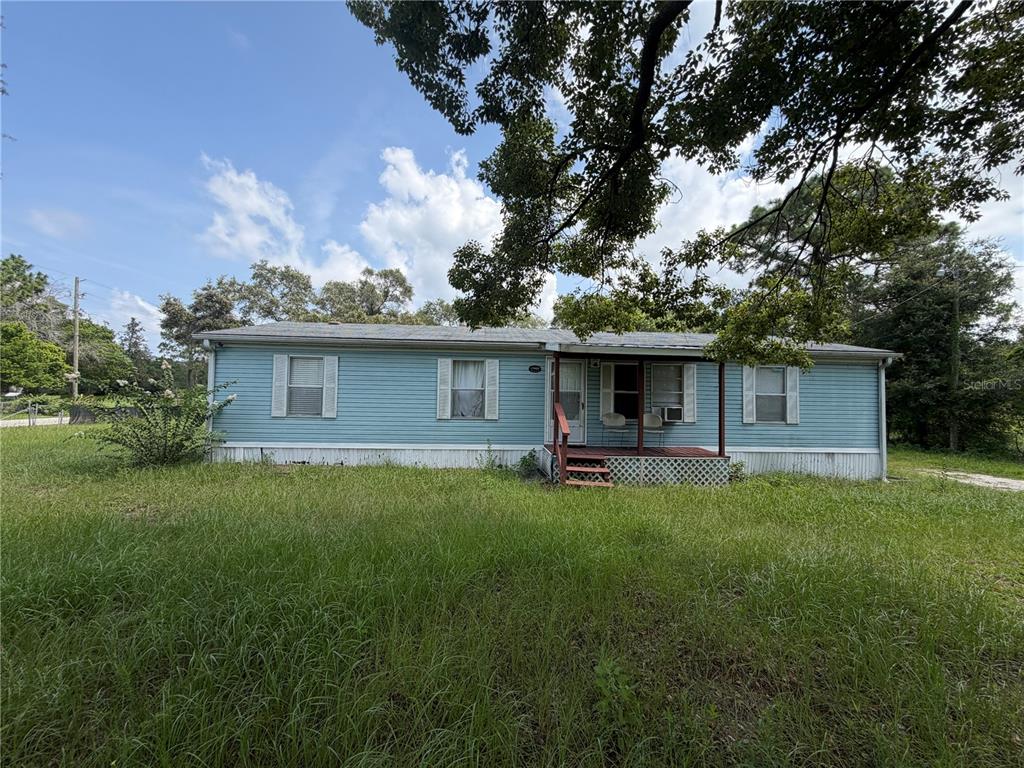 A light blue single-wide mobile home sits on a grassy lot under large trees — 17828 ALEXSON STREET, SPRING HILL, FL