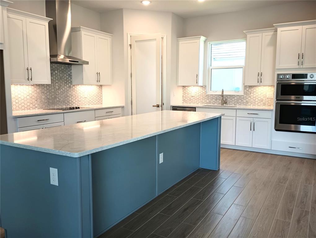A kitchen features white cabinets, a blue island, stainless steel appliances, and a tiled backsplash — 134 NEW LEATHERWOOD DRIVE, PALM COAST, FL