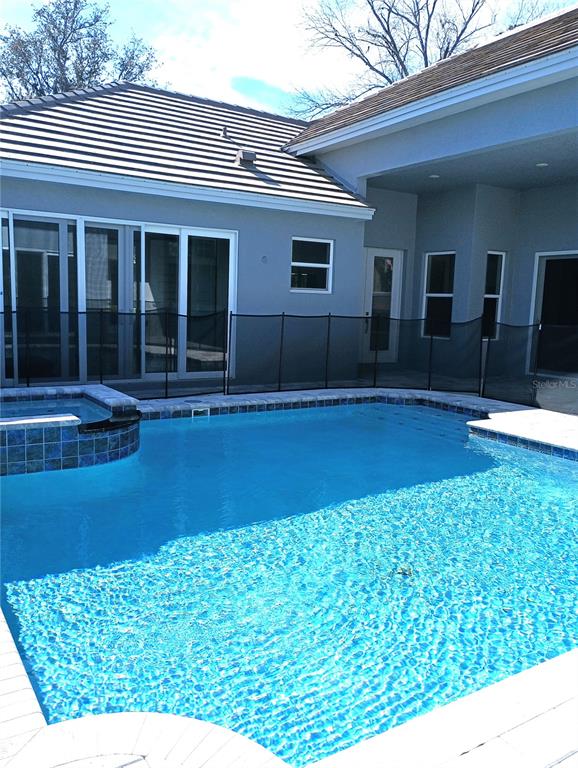 A swimming pool with a tiled spa sits in front of a gray house exterior — 134 NEW LEATHERWOOD DRIVE, PALM COAST, FL