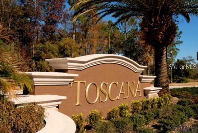 A brown monument sign with gold lettering reads Toscana, situated near a palm tree — 134 NEW LEATHERWOOD DRIVE, PALM COAST, FL