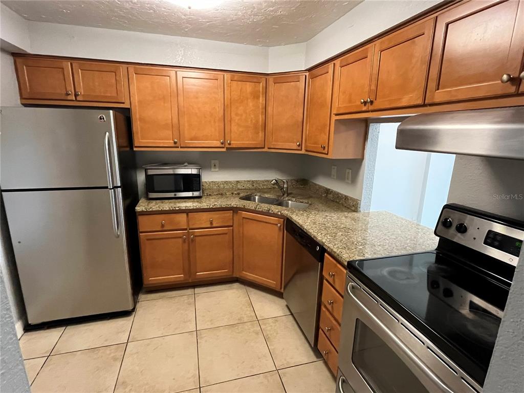 A kitchen features wood cabinets, granite countertops, stainless steel appliances, and light-colored tile flooring — 2610 COCONUT BAY LN LANE UNIT 733, SARASOTA, FL