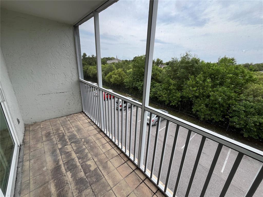 A screened-in balcony with tiled flooring overlooks a parking lot and trees — 2610 COCONUT BAY LN LANE UNIT 733, SARASOTA, FL