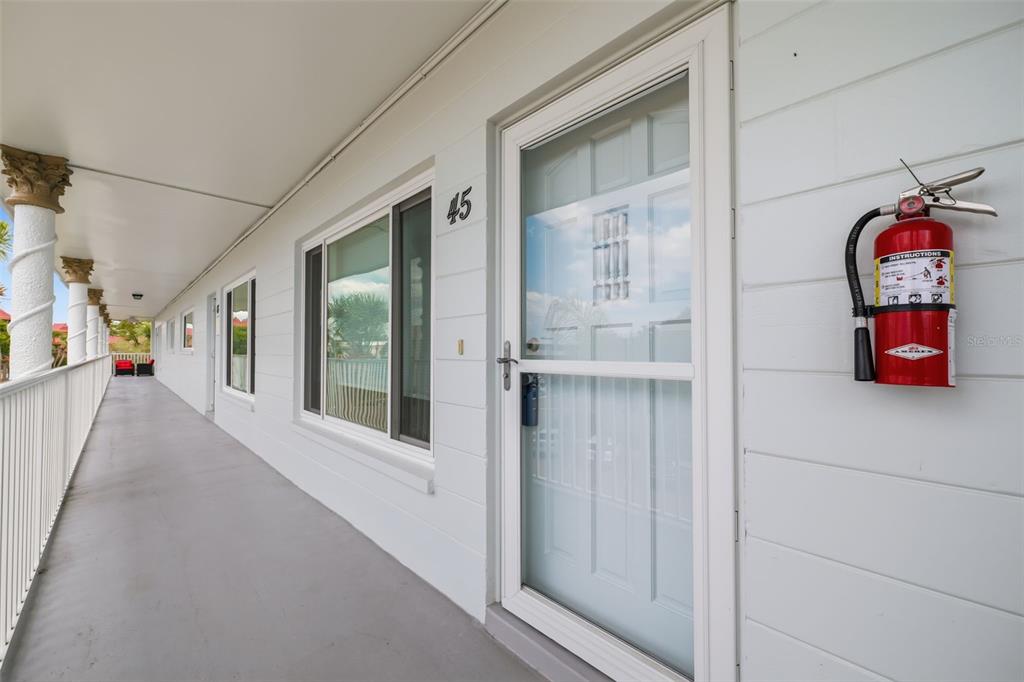 An exterior walkway features white siding, a numbered door, and a wall-mounted fire extinguisher — 2381 ECUADORIAN WAY UNIT 45, CLEARWATER, FL