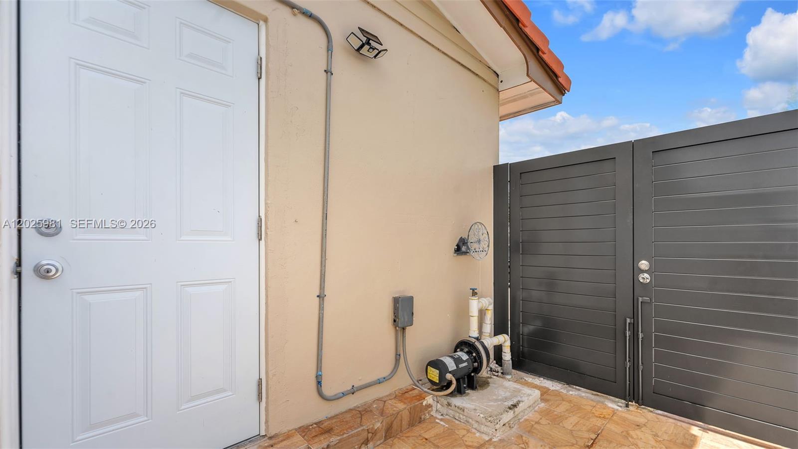 A white door, a pool pump, and a dark gate are on a tiled patio — MIAMI, FL