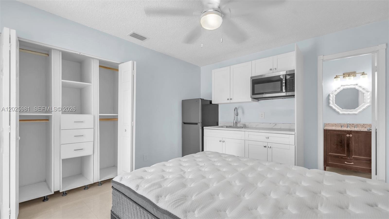 A bedroom features a kitchenette with white cabinets, a microwave, and an attached bathroom — MIAMI, FL