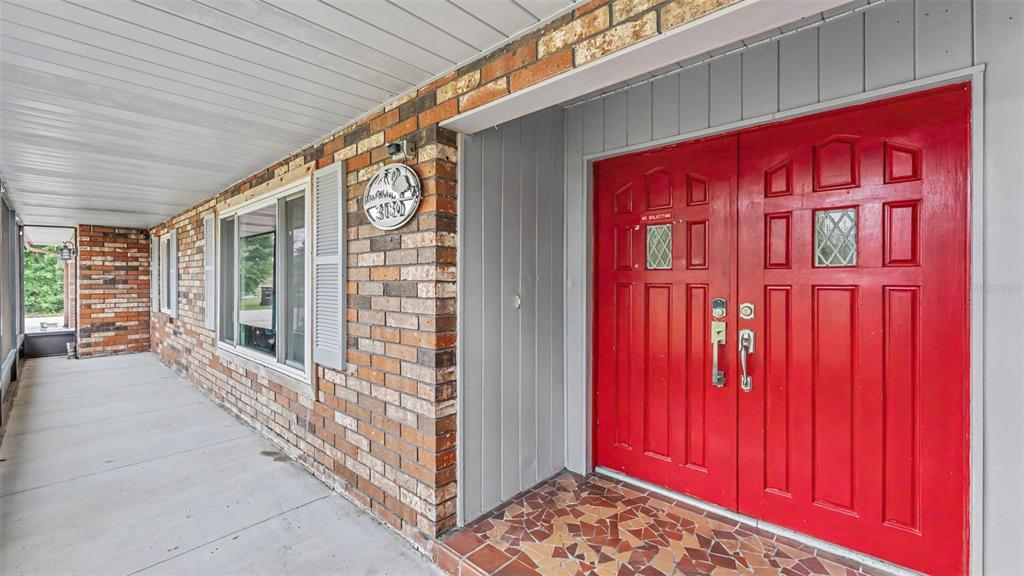 A brick exterior house features a covered porch and a bright red double front door — 3180 FLAMINGO LANE, MULBERRY, FL