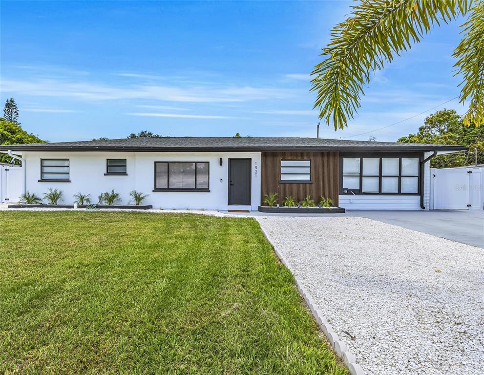 A single-story house features a white exterior, wood-slat siding, a gravel driveway, and a lawn — 1921 FERN AVENUE, SARASOTA, FL