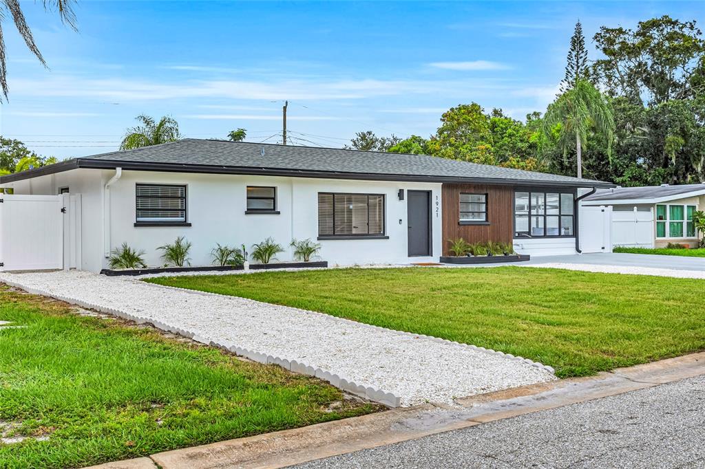 A single-story house with white stucco, wood siding, a gravel driveway, and a green lawn — 1921 FERN AVENUE, SARASOTA, FL