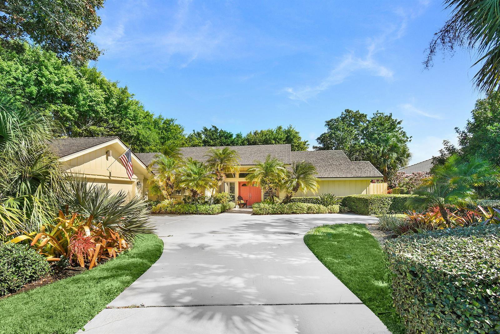A single-story house with a beige exterior, a red front door, and a concrete driveway — 6111 SE Winged Foot Drive, Stuart FL 34997, STUART, FL