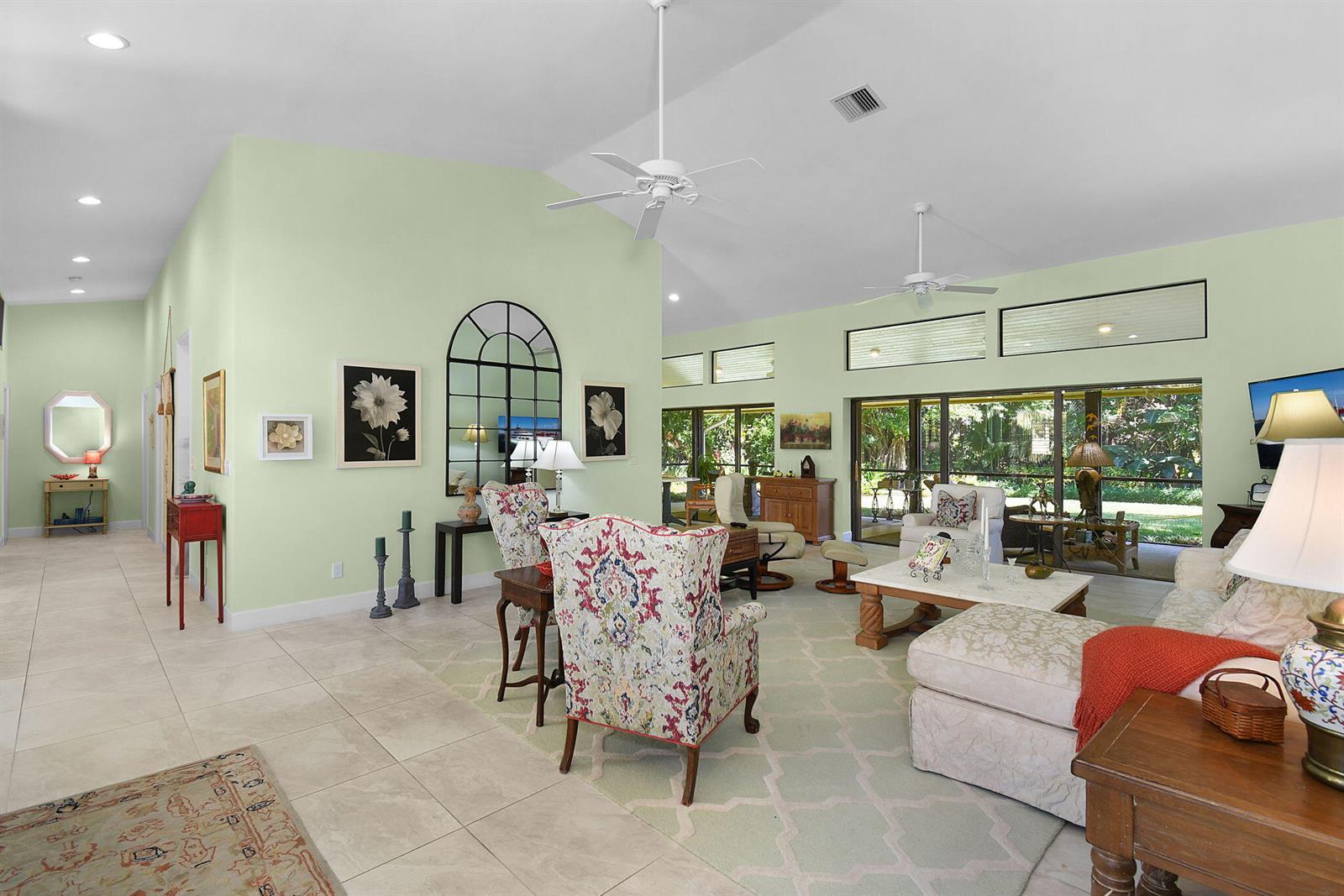 A spacious living room features light green walls, vaulted ceilings, tile floors, and large windows — 6111 SE Winged Foot Drive, Stuart FL 34997, STUART, FL