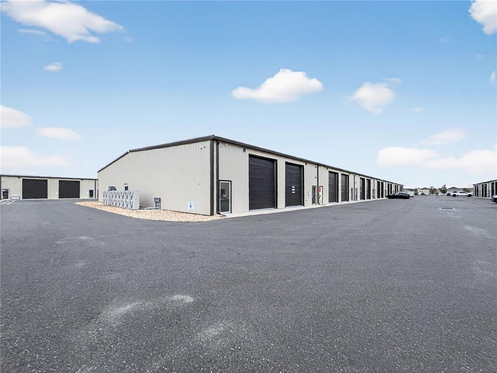A long, metal-sided commercial warehouse building features multiple roll-up doors and a paved parking lot — 4707 COUNTY ROAD 156, WILDWOOD, FL