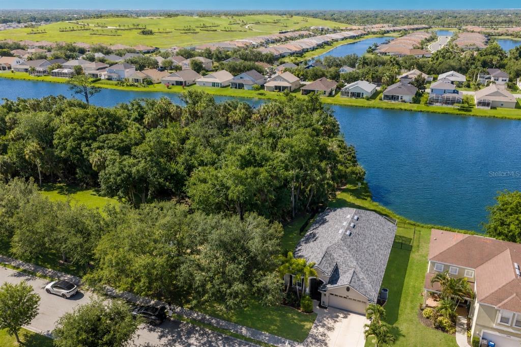 An aerial view shows a house with a gray roof next to a large lake — 5030 58TH TERRACE E, BRADENTON, FL