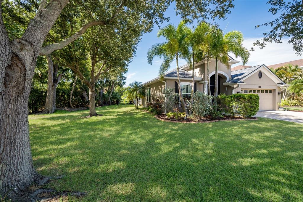 A single-story house with a tan exterior, palm trees, and a large grassy front yard — 5030 58TH TERRACE E, BRADENTON, FL