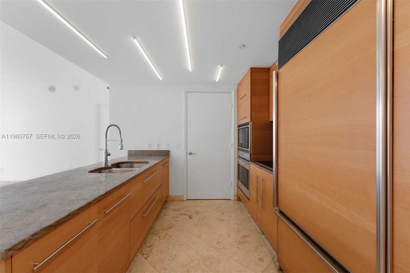 A kitchen features wood cabinetry, stone countertops, a double sink, and recessed linear lighting — 475 Brickell Ave # 3513, Miami FL 33131, MIAMI, FL