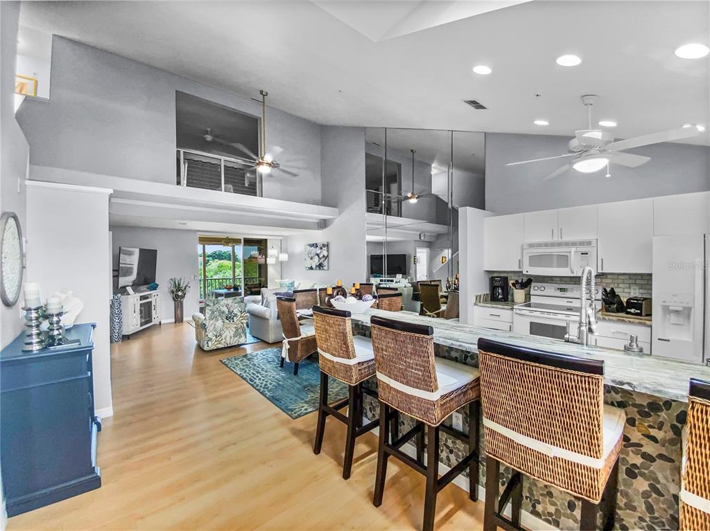 An open-concept kitchen and living area features a breakfast bar, vaulted ceilings, and light flooring — 8370 WINGATE DRIVE UNIT 725, SARASOTA, FL