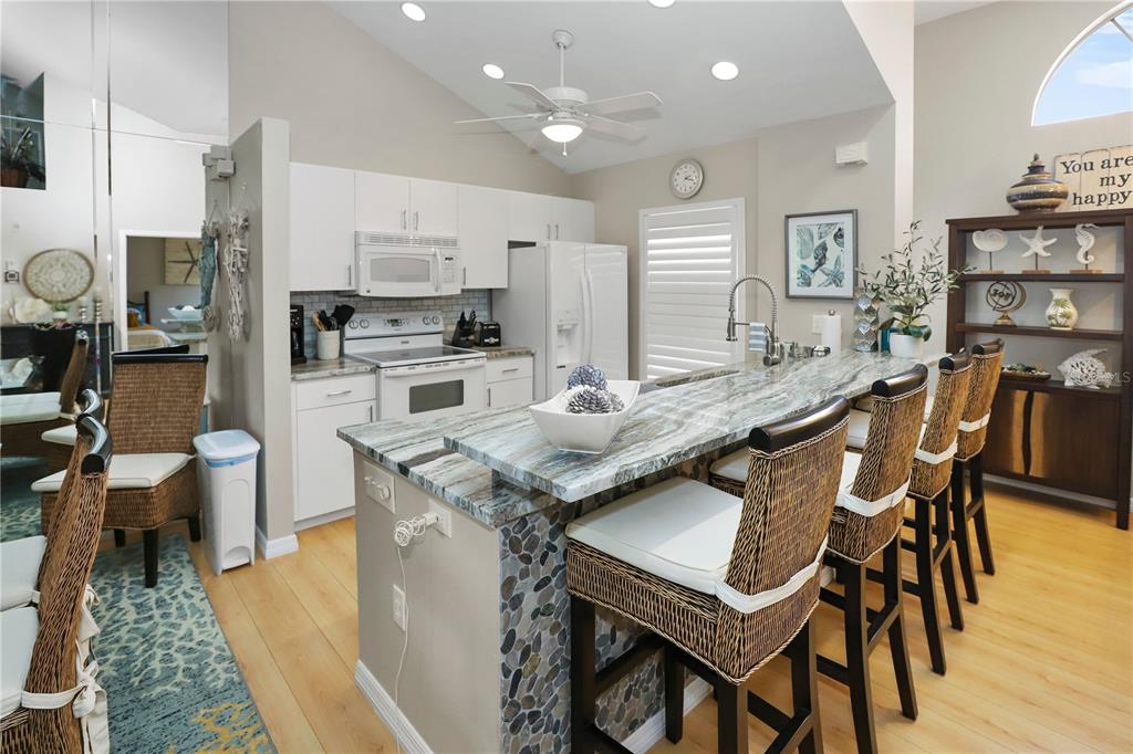A kitchen features white cabinetry, stone-topped island seating, and light wood flooring — 8370 WINGATE DRIVE UNIT 725, SARASOTA, FL