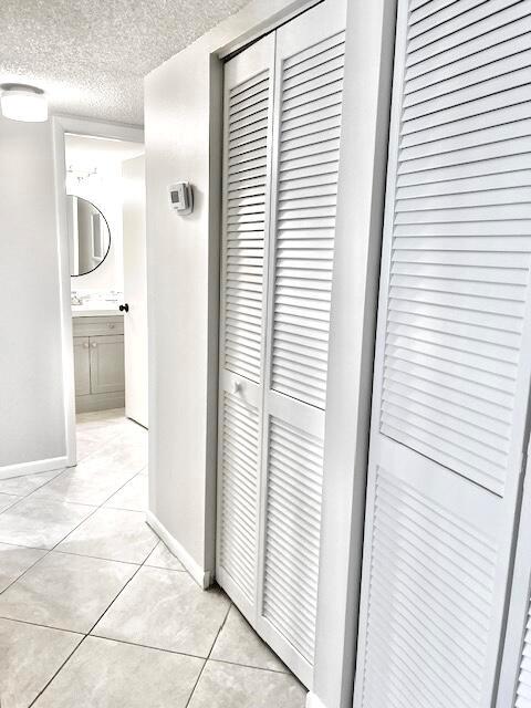 A hallway with light tile flooring leads to a bathroom featuring white louvered closet doors — 1605 S Us Hwy 1 # A106, Jupiter FL 33477, JUPITER, FL