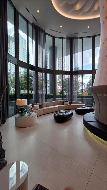 A modern living room features floor-to-ceiling windows, a curved sofa, and a large fireplace — 100 1ST AVENUE N UNIT 2406, ST PETERSBURG, FL