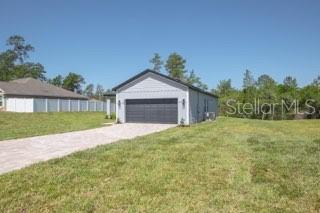 A detached gray garage with a dark door sits on a grassy lot — 604 MARION OAKS LANE, OCALA, FL
