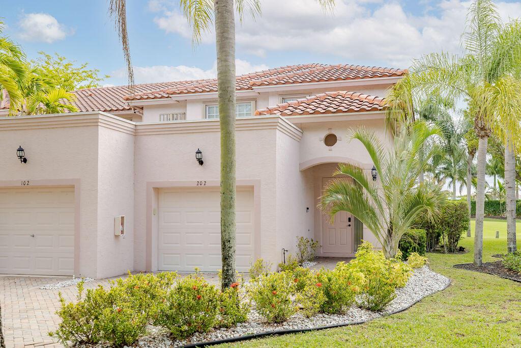 A two-story stucco townhouse features two garage doors, a covered entryway, and palm trees — 8050 Aberdeen Drive # 202, Boynton Beach FL 33472, BOYNTON BEACH, FL
