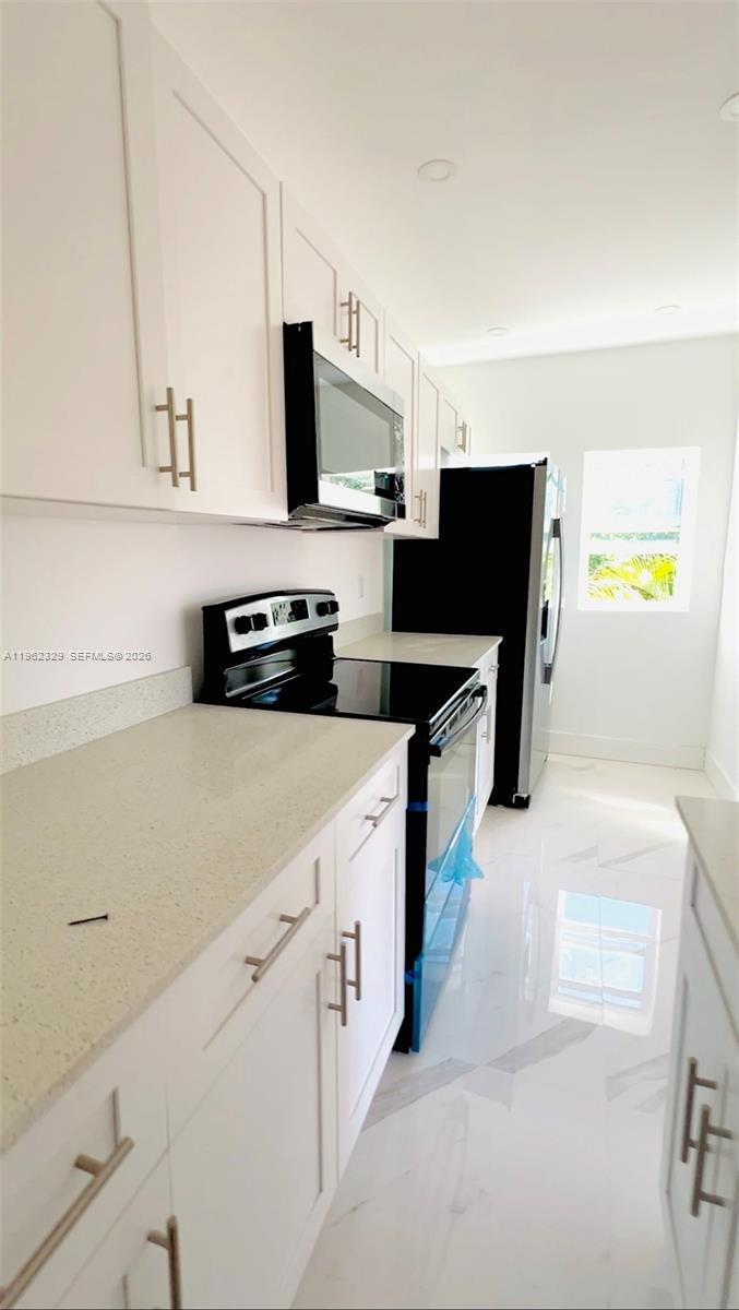 A modern kitchen features white cabinets, light countertops, and black appliances on a tiled floor — 1015 S 17th Ave # 11, Hollywood FL 33020, HOLLYWOOD, FL
