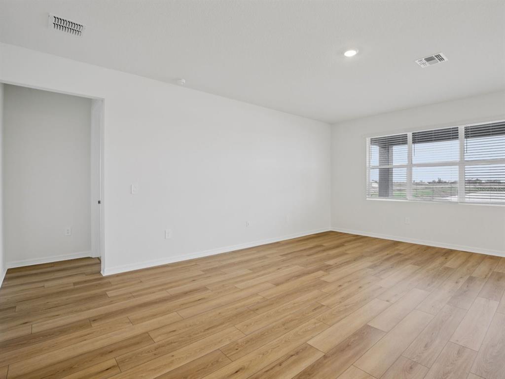 An empty room with white walls, light wood-look flooring, and a large window — 9013 VENETIA COURT, PALMETTO, FL