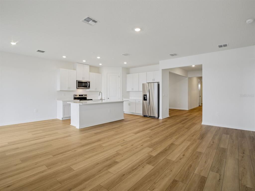 A bright, open-concept kitchen features white cabinetry, stainless steel appliances, and light wood-look flooring — 9013 VENETIA COURT, PALMETTO, FL