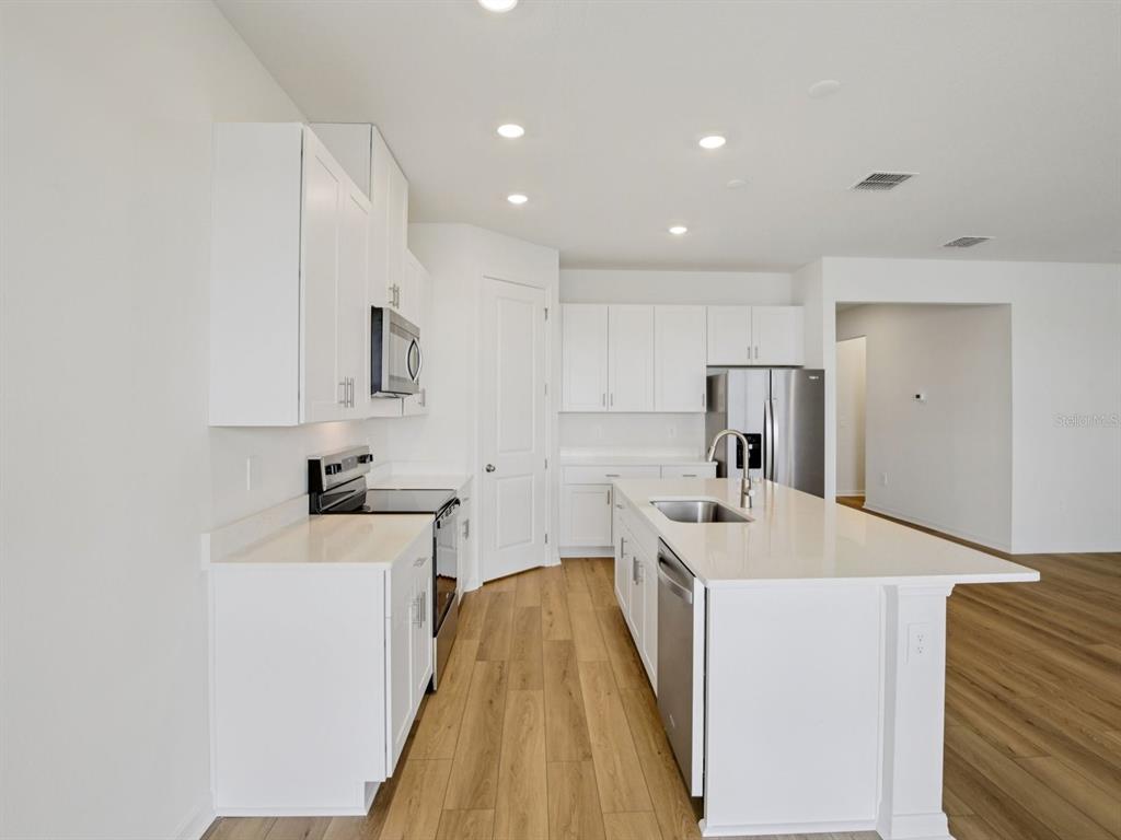 A modern kitchen features white cabinetry, quartz countertops, stainless steel appliances, and light wood flooring — 9013 VENETIA COURT, PALMETTO, FL