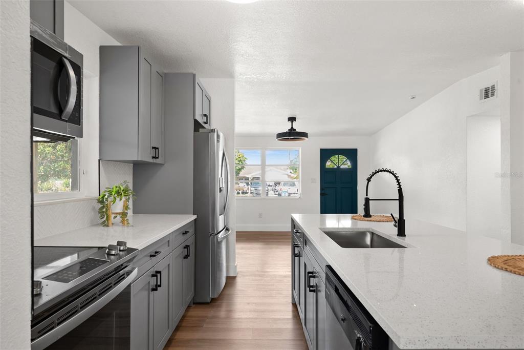 A modern kitchen features gray cabinets, white countertops, stainless steel appliances, and a central island — 9596 GROVELAND STREET, SEMINOLE, FL